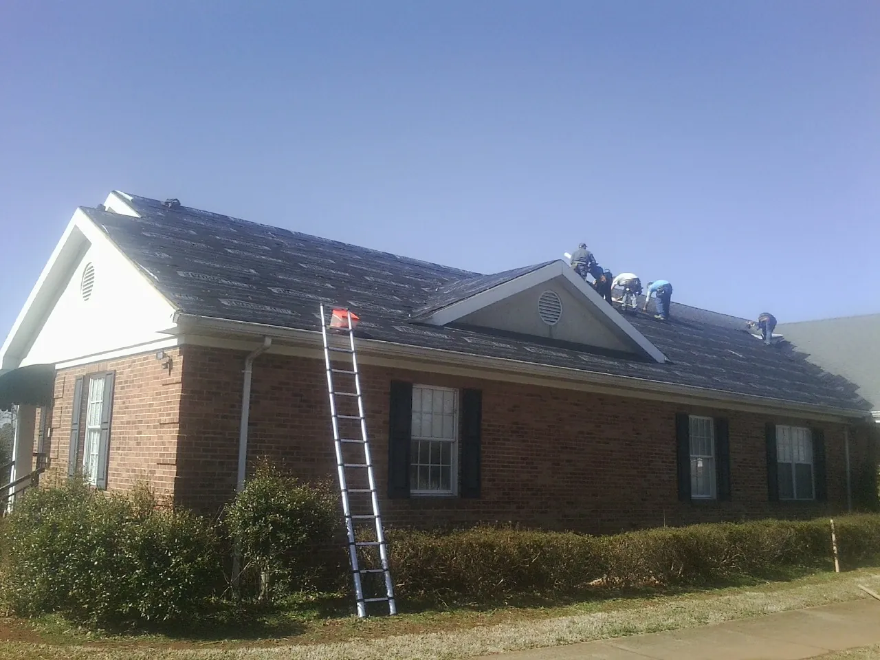 Crew tearing shingles off a brick ranch roof with a ladder set — Emergency Roof Repair work by our crew in Pulteney