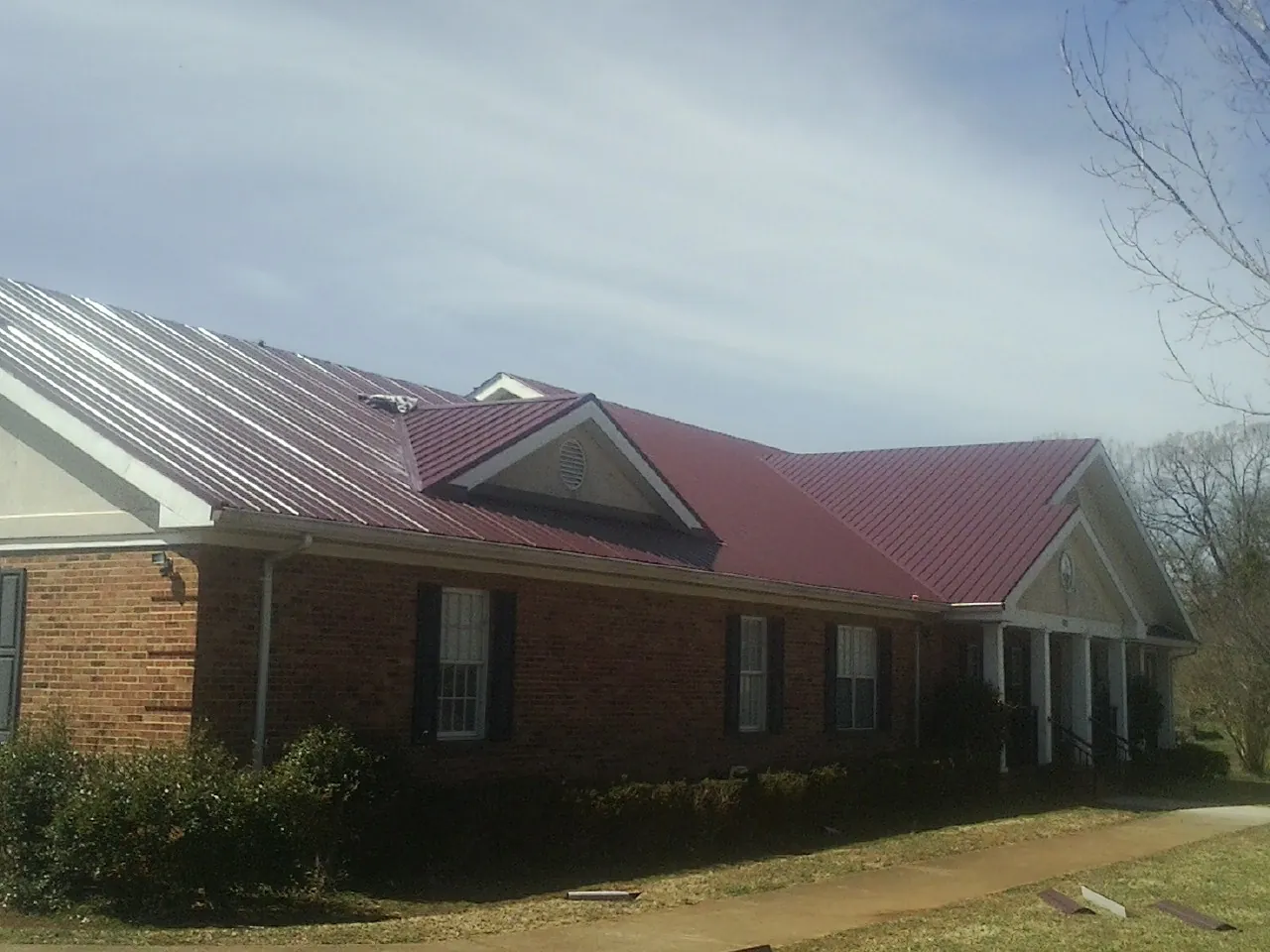 Red metal roof with gabled entries on a long brick building, from a Hail Damage Roof Repair job in Pulteney