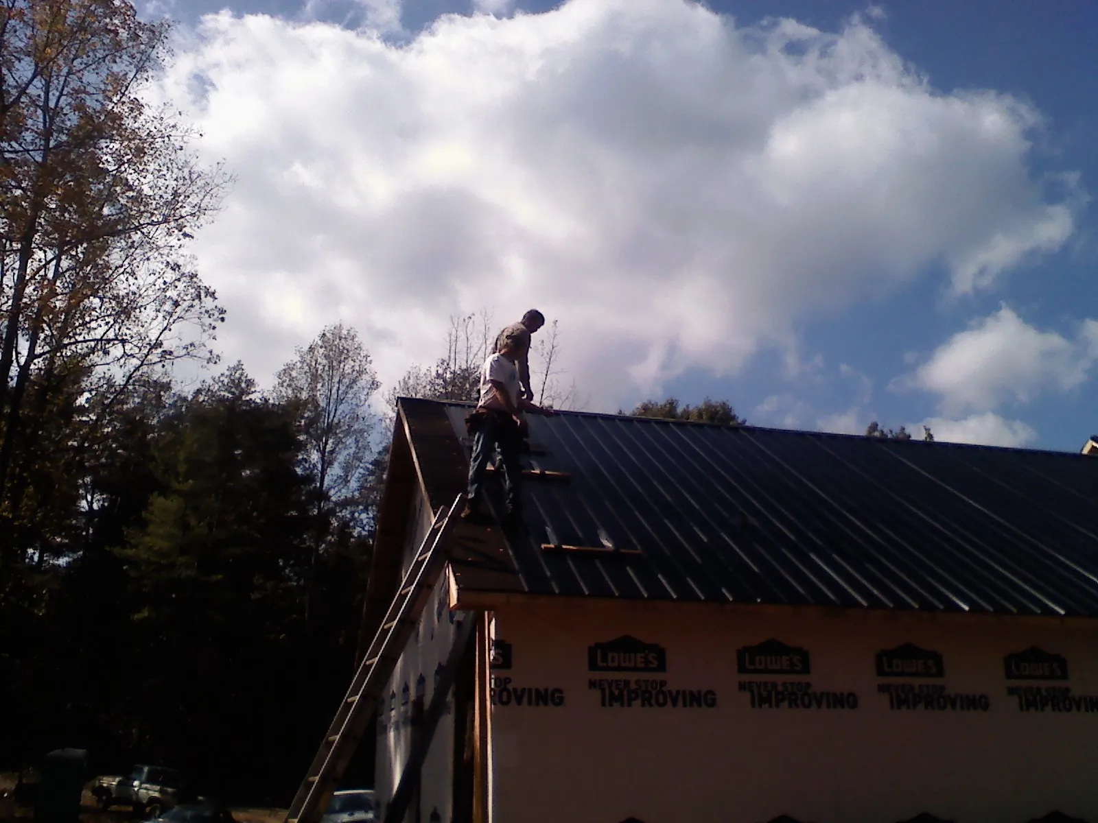 Roofer fastening dark metal panels high against a cloudy sky, from a Roof Inspection job in Pulteney