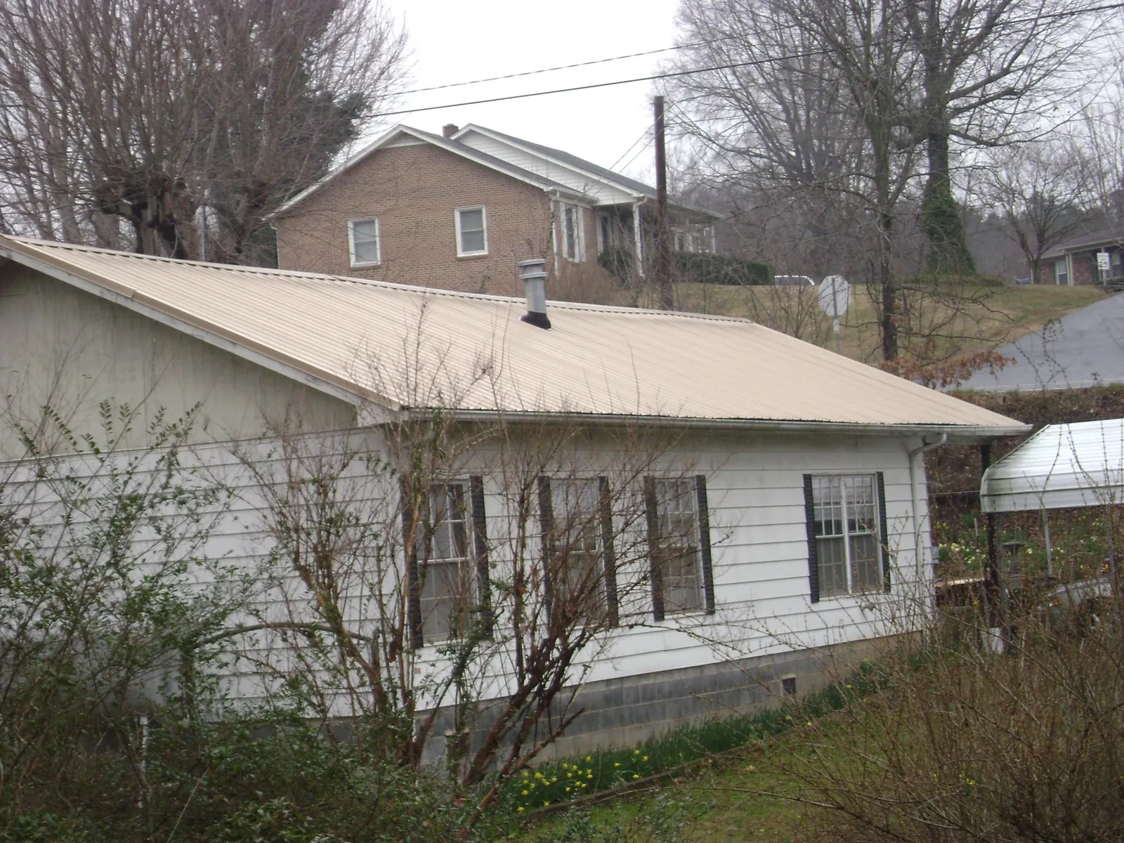 Tan metal roof on a white sided house set into a hillside — Commercial Roofing by Roofing Brothers in Pulteney