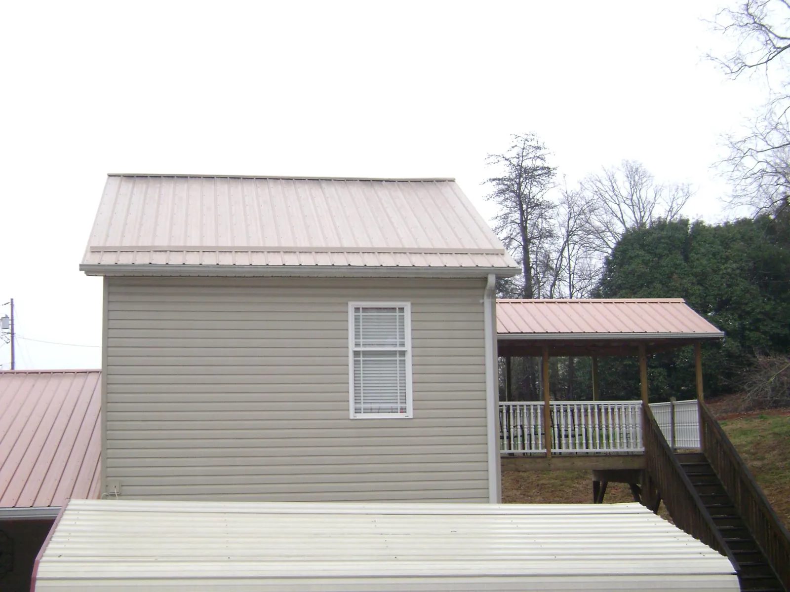Tan metal roofs on a two story addition and attached porch, from a Roof Replacement job in Pulteney